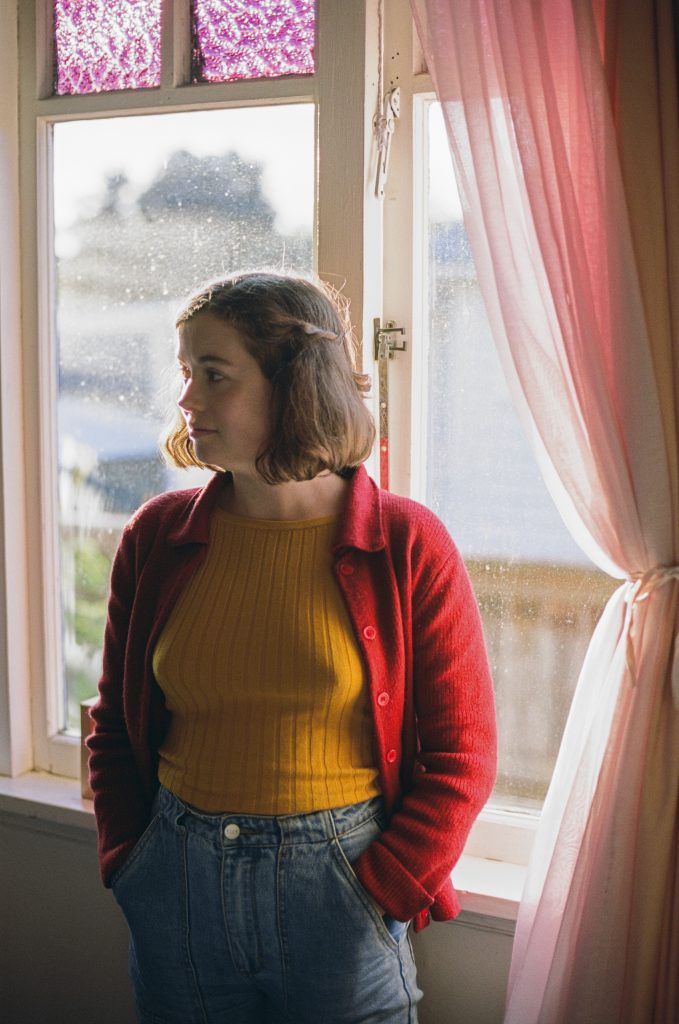 Clare in yellow standing beside a window Clare in yellow standing beside a window