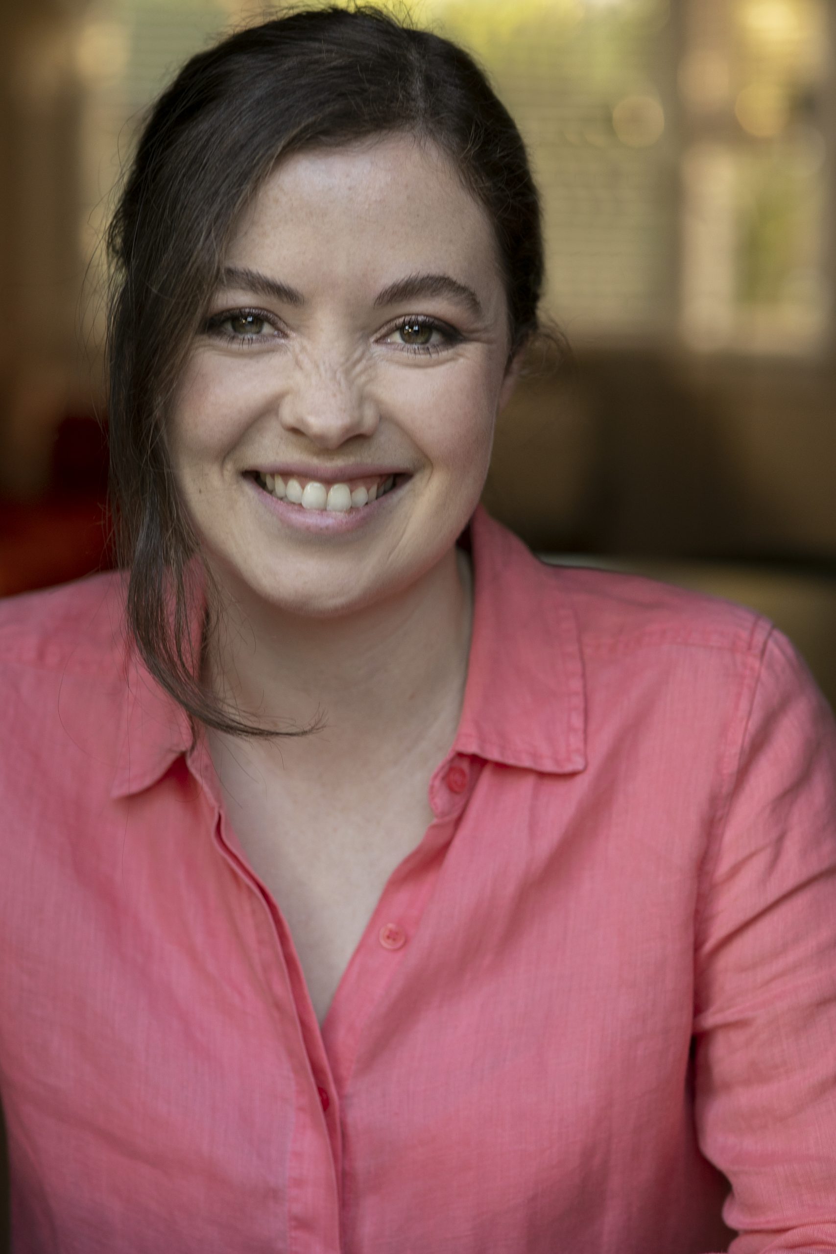 Clare wears a pink shirt and grins warmly