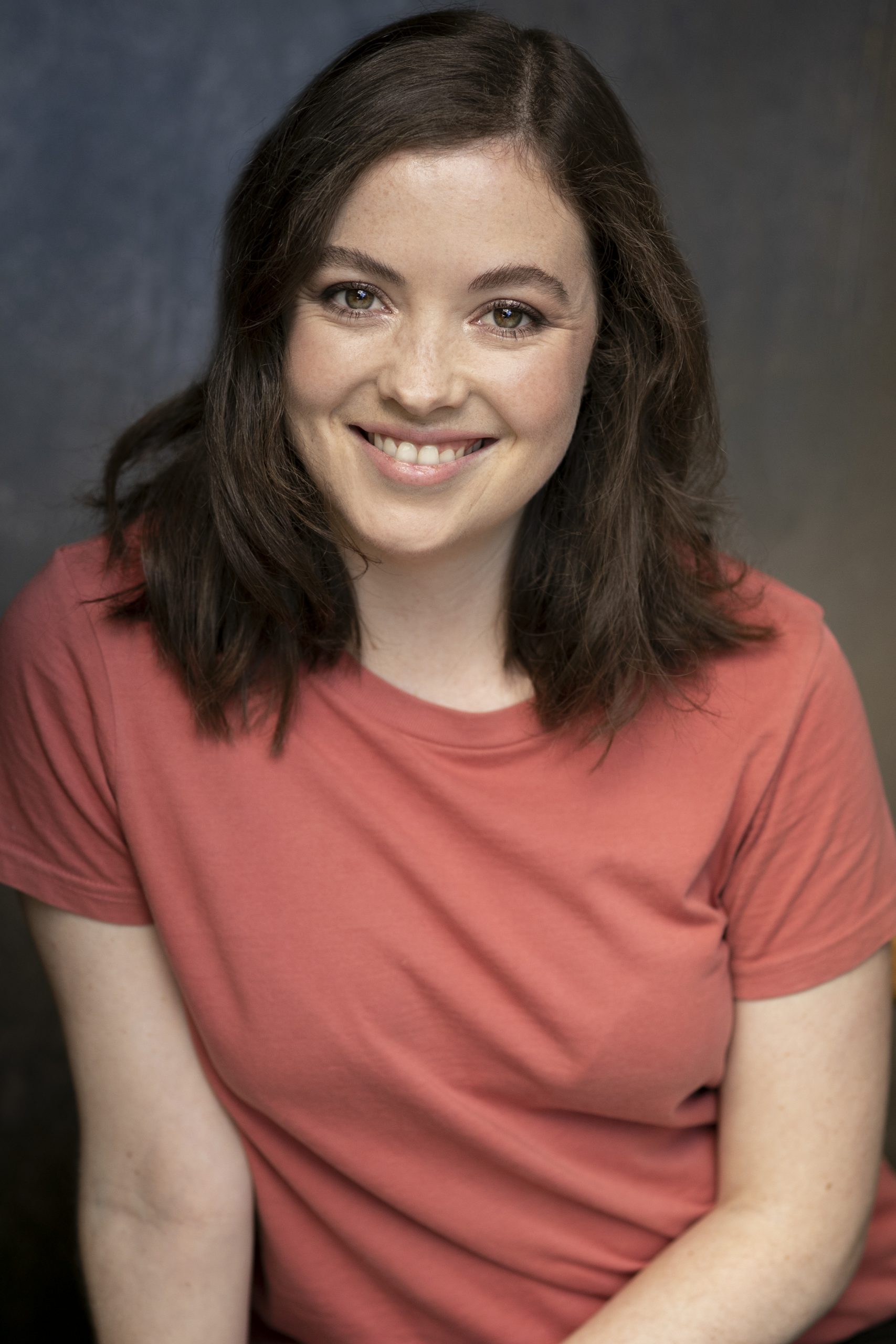 Clare grinning warmly in a dark blush pink tshirt