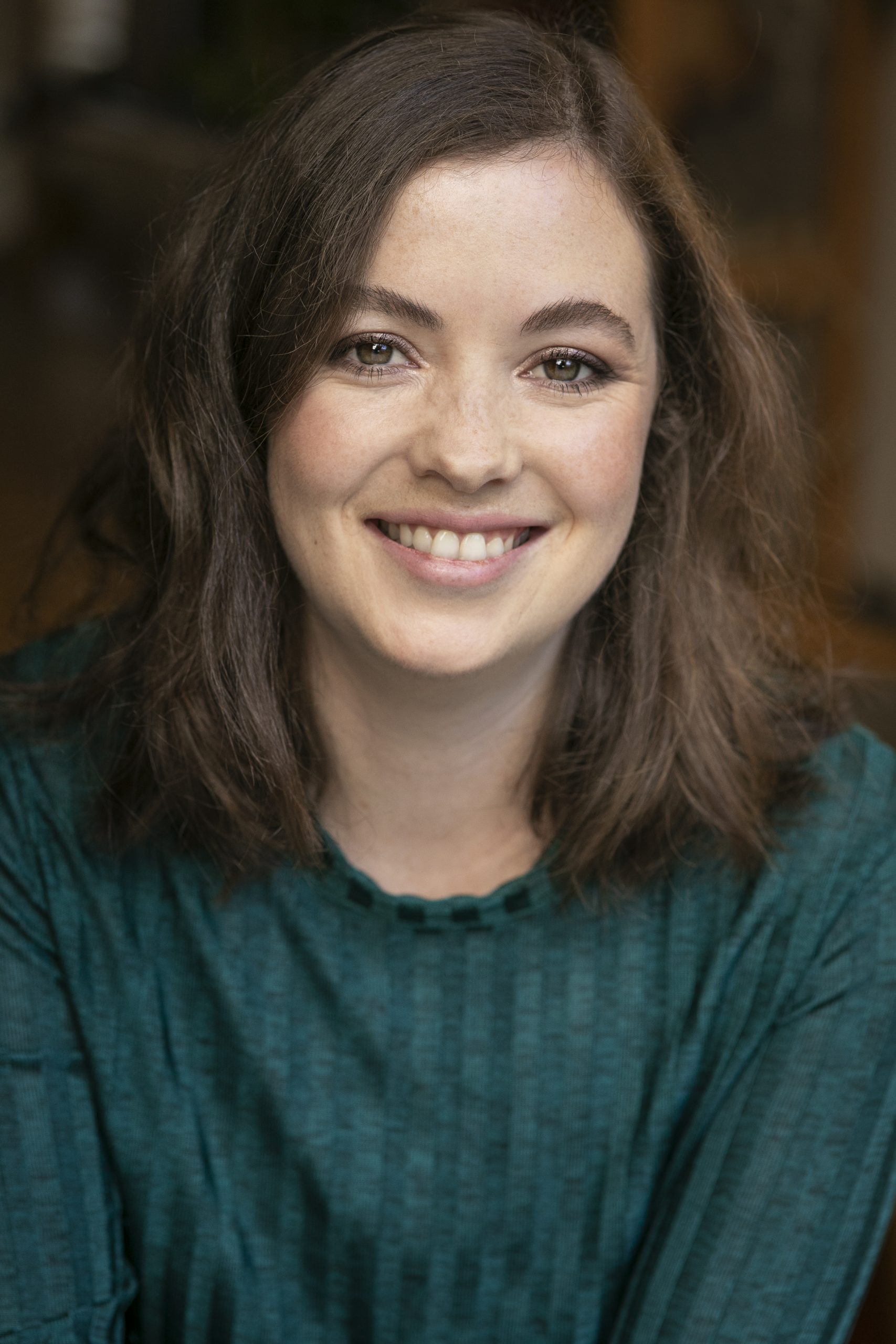 Photo of brunette Clare Marcie in a teal long sleeved top smiling warmly