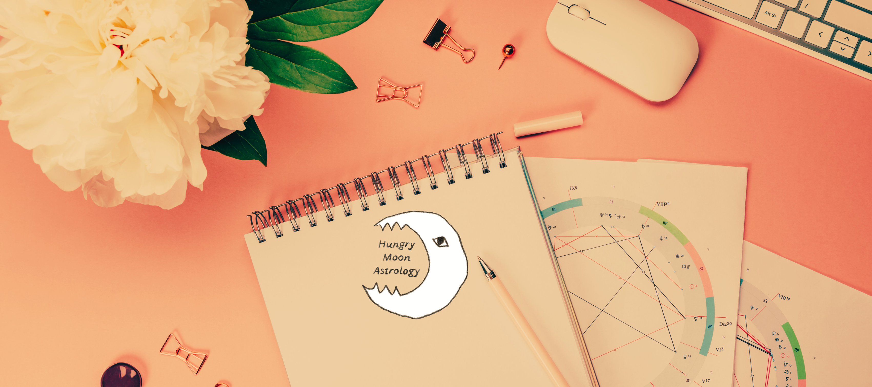 Hungry Moon logo on a notepad beside birth charts, a mouse and laptop and a bunch of flowers