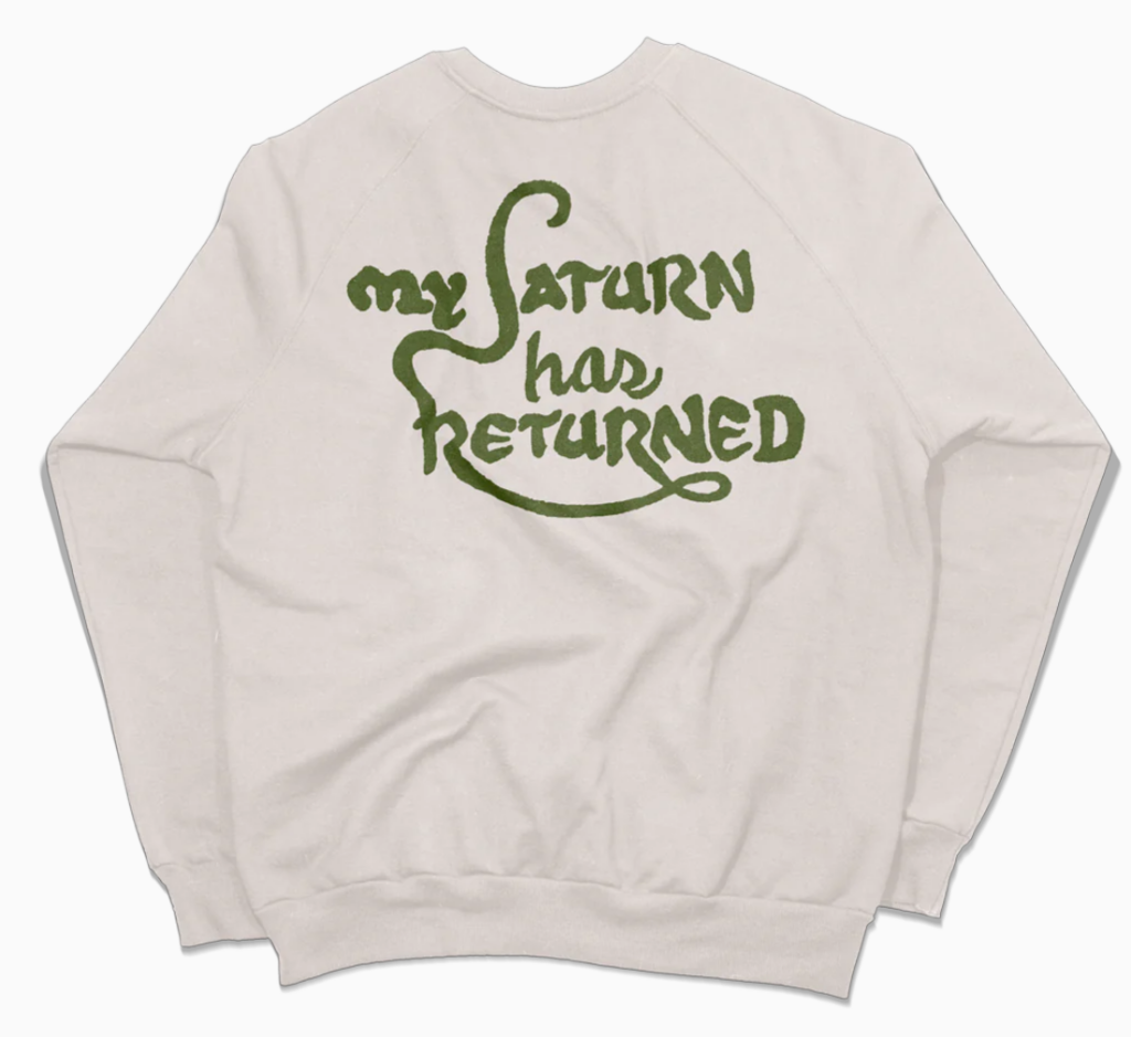 the back of a Kacey Musgraves sweater for sale featuring swirling green text reading: "My Saturn has returned"