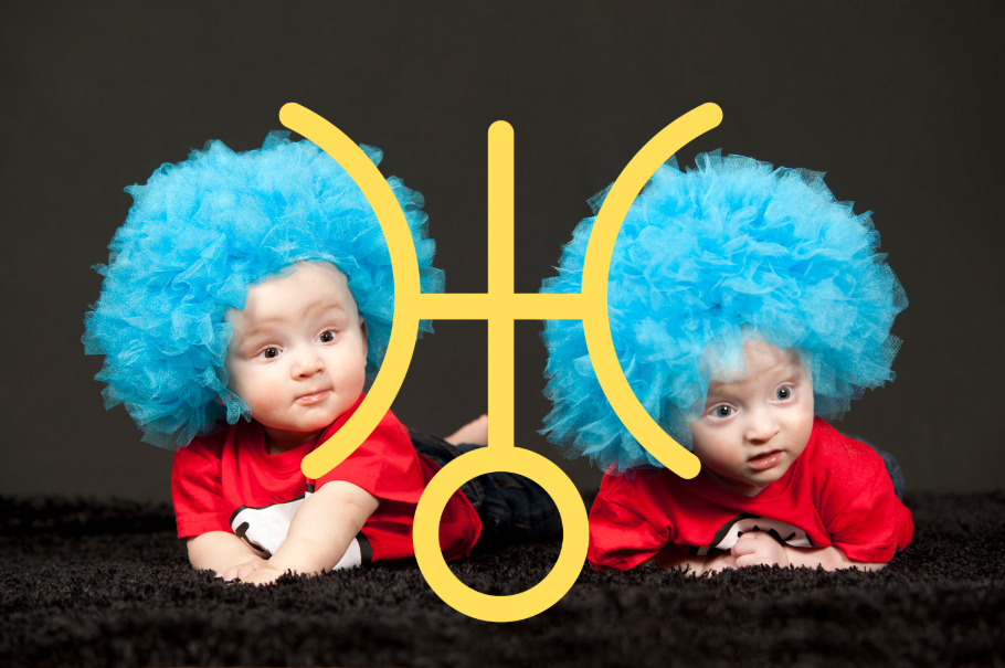 two babies lie propped up on their tummies wearing matching blue tulle wigs and looking surprised, between them a large yellow symbol for uranus